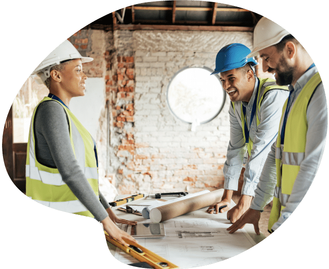 Three construction workers discussing plans at a worksite table.