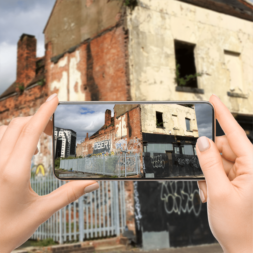Hands holding a phone, showing a photo of a graffiti-covered, abandoned building.