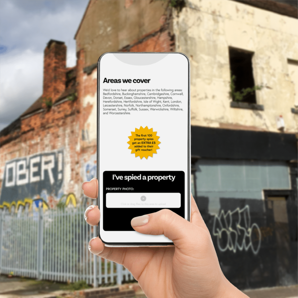 Hand holding a phone displaying the propertyspy website, with an abandoned building in the background.