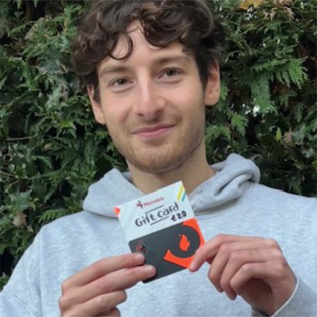 Person holding a £20 Nando's gift card in front of green foliage.