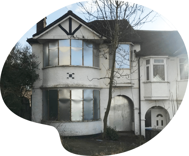 An abandoned, boarded-up white house with a gabled roof and overgrown yard.